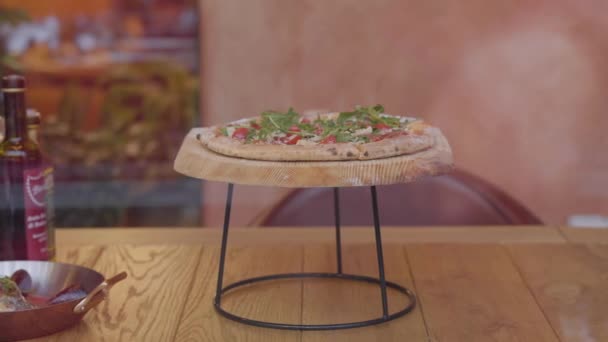 Die leckere Pizza liegt auf einem Holzständer auf dem Tisch im Restaurant. Konzept des Abendessens. — Stockvideo