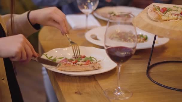 Unrecognizable couple eating pizza with fork and knife and drinking wine in modern italian cafe at the table. Man and woman have a date in restaurant. Camera moves up — Stock Video