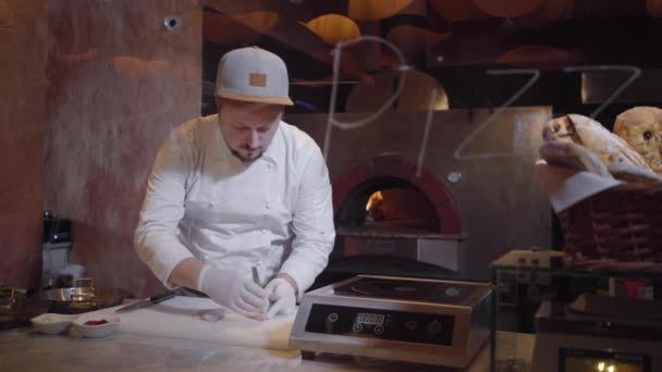 Giovane in uniforme da chef che prepara pesce crudo sul tagliere. Cook tira fuori le ossa dal filetto usando delle pinze. Preparazione del cibo nel ristorante, frutti di mare. Sparare dietro il vetro con firme — Video Stock