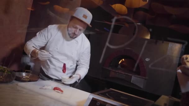 Cozinheiro profissional em jaqueta branca e cozinheiros de borracha fazendo um sanduíche com peixe vermelho na cozinha do restaurante. O chef prepara deliciosos lanches . — Vídeo de Stock