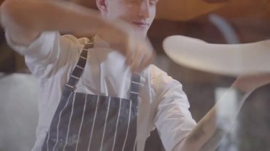 Usta hamur modern restoran mutfak pişirme pizza Maker olumlu yakın çekim. Pizza hamur ve prinkling çevresinde lokanta mutfağı un ile iplik Şef üniformalı genç gülümseyen adam.
