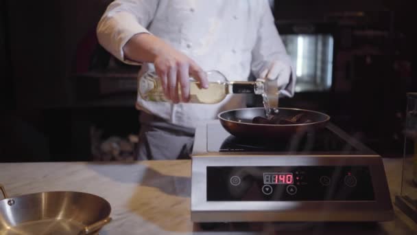 Unrecognizable chef in white uniform and rubber glove pouring white wine in the frying pan, cooking mussels in modern restaurant close up. Process of food preparing — Stock Video