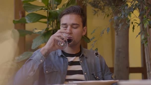 Portrait d'un type séduisant buvant du vin avec un verre de vin assis à une table dans un restaurant. Jeune homme appréciant en attendant un délicieux dîner. Effet de réfraction de la lumière. Mouvement lent . — Video