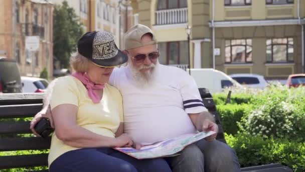 Retrato de casal velho elegante de viajantes sentam-se no banco em cidade estrangeira olhando para o mapa — Vídeo de Stock