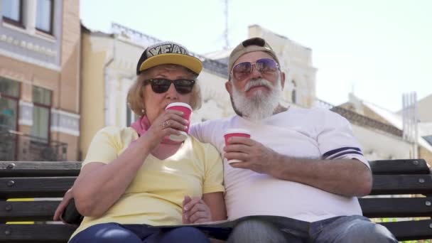 スタイリッシュな年配のカップルの肖像画を飲むコーヒーと市のベンチでリラックス — ストック動画