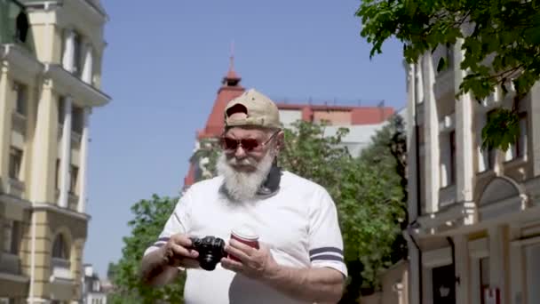 Porträtt av stilig gubbe i keps och solglasögon ta foto promenader i staden — Stockvideo