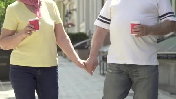 Senioren spazieren mit Händchen und Kaffee durch die Stadt — Stockvideo