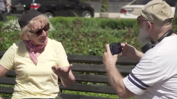 Stilvolles reifes Paar schaut die Fotos vor laufender Kamera auf der Bank im Park an — Stockvideo