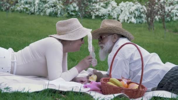 Äldre par utfodring varandra marshmallows på picknick i parken — Stockvideo