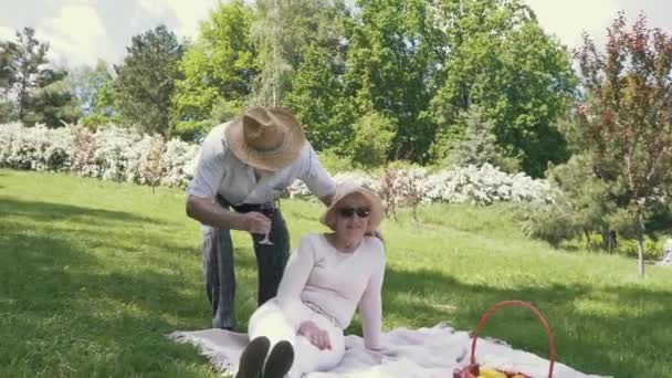 Старший чоловік у капелюсі приносить келих вина своїй милій дружині — стокове відео