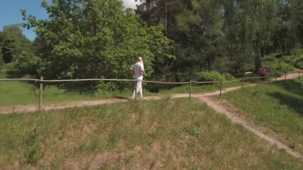 Hombre mayor corriendo con su esposa en el parque de verano por la mañana. Disparando desde el dron . — Vídeos de Stock