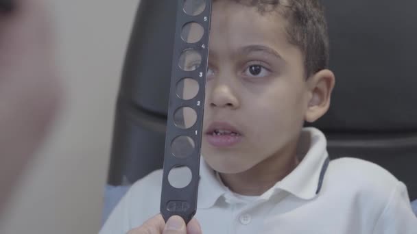 Szép afro-amerikai fiú ül a székre, a szemész orvos arcképe. Szakmai szemész a látás a gyermek ellenőrzi. Szemvizsgálat. Lassú mozgás — Stock videók