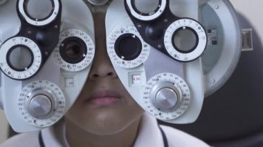 Küçük çocuklar göz muayenesinde, optometrist göz doktoruna phoropter kullanarak kapatın. Sevimli genç melez çocuk phoropter yanıp sönen camdan bakıyor. Ağır çekim
