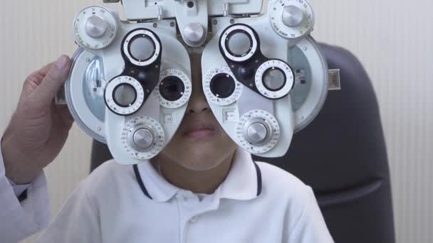 Optometrist examencommissie mannelijke patiënt op phoropter in oogheelkunde kliniek. Afro-Amerikaanse jongen doen oogtest. Slow motion. — Stockvideo