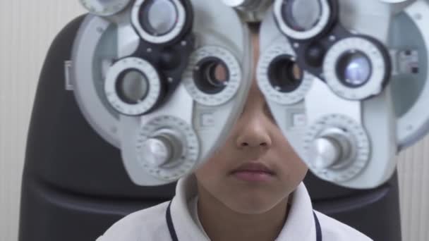 Kleine Jungen Augenuntersuchung beim Augenarzt mit dem Phoropter aus nächster Nähe. Hände eines Arztes im weißen Arztkittel legen Phoropter in die Augen eines Teenie-Mulatten — Stockvideo