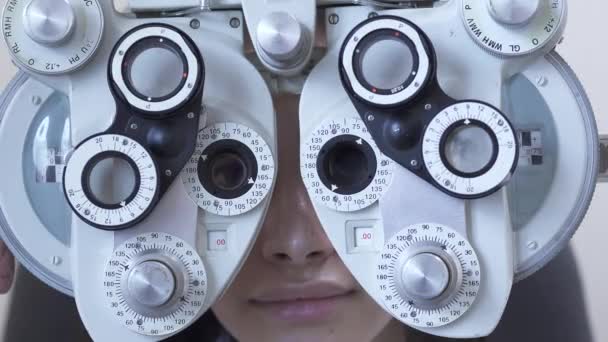 Jonge vrouw examen van de ogen van optometrist oogarts met behulp van phoropter close-up. Leuke vrouw glimlacht op zoek via glas van optometrie machine. Hand van de arts veranderen van glas. Slow motion — Stockvideo