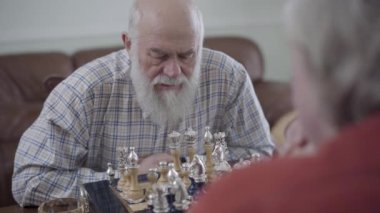 Evde deri kanepede oturan satranç oynayan iki eski insanlar. Sakallı adam bir hareket yapma. Beyaz yaşlı adamlar komşular arkadaşlar sevinçle kapalı satranç