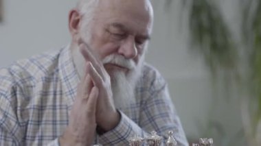 Bir hamle yapmak için hangi satranç taşını düşünme sakallı yaşlı olgun adam portresi. Evde deri kanepede oturan satranç oynayan iki insanlar. Komuta sizde stratejik, ellerini ovuşturarak düşünüyor