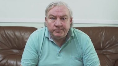 Uzaktan kumanda aletini kullanarak kanalları Tv. yaşlı adam geçer izlerken kahverengi deri kanepede oturan mavi t-shirt portre olgun tombul adam. Boş zaman emekli