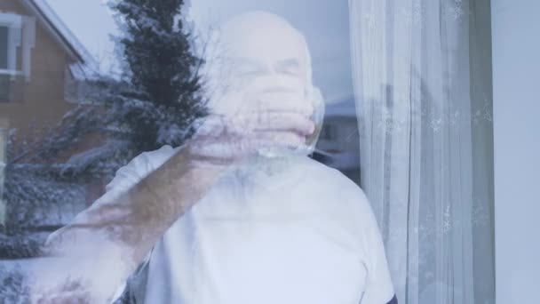Vousatý starý muž pít alkohol whiskey stojící u okna doma. Kavkazská stařec stráveném času uvnitř, mimo. Volný čas důchodce. Střelba zpoza skla — Stock video