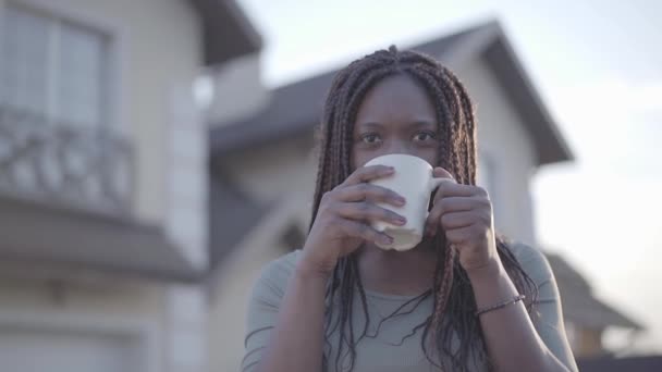 Magabiztos afrikai-amerikai fiatal fekete mosolygó nő portréja forró csésze kávéval az utcán. Lassú mozgás — Stock videók