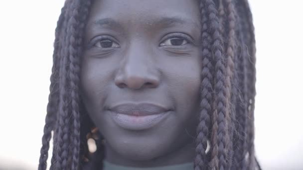 Close-up van portret van vertrouwen Afro-Amerikaanse jonge zwarte lachende vrouw op de achtergrond van de hemel en straat. — Stockvideo