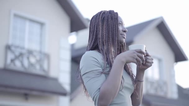 Portrait d'une jeune femme afro-américaine assez confiante et souriante noire avec une tasse de café chaude dans la rue. Mouvement lent — Video