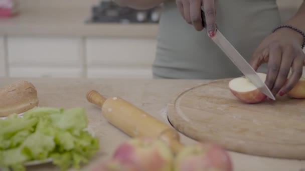 Afrikalı-Amerikalı kadın kesme apple ile modern mutfak arka plan üzerinde ahşap tahta üzerinde bıçak. Yakın çekim — Stok video