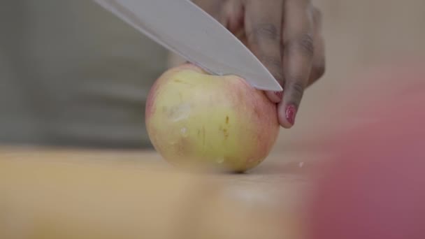 Africká americká žena řezání chutné šťavnaté jablko s nožem na dřevěné desce na kousky. Detailní záběr