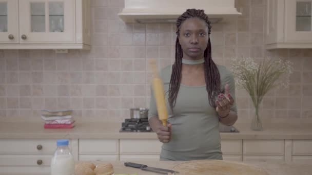 Belle femme africaine américaine debout avec rouleau à pâtisserie et penser à la préparation de tarte sur le fond de la cuisine moderne. Mouvement lent — Video