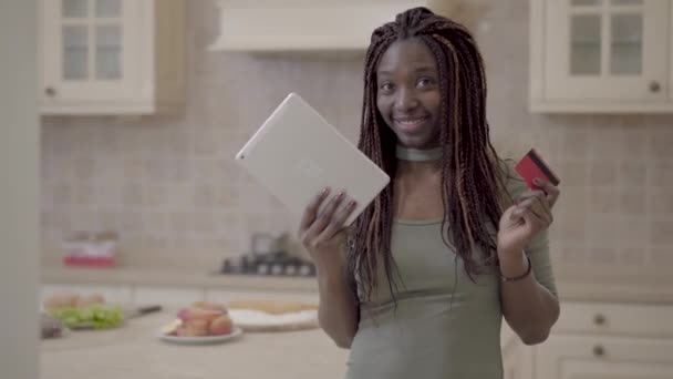 Портрет красивой африканской улыбающейся женщины, принимающей таблетки и кредитные карты после успешной транзакции в Интернете — стоковое видео