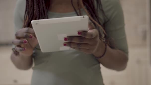 Vista de cerca de las manos de mujer afroamericana sosteniendo tableta blanca gadget navegar por Internet, charlando con amigos, leyendo noticias en línea. Ocio de la joven en casa. Cámara mueve a la izquierda — Vídeo de stock