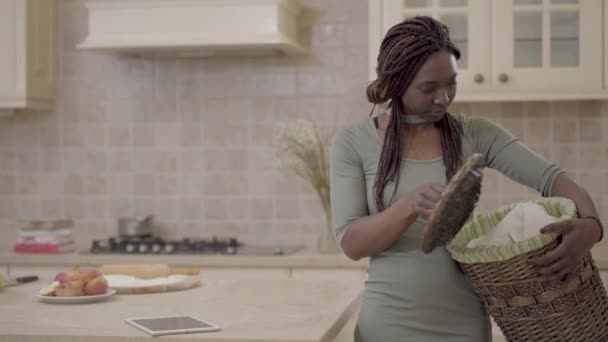 Africano americano mulher cansado bonita jovem mulher com sujo lavanderia cesta de pé na cozinha e pensar sobre a limpeza da casa — Vídeo de Stock