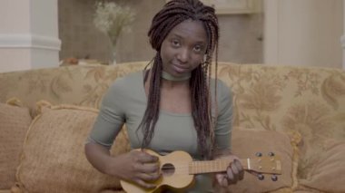 Modern oturma odasında Koç Tarih ukulele gitar çalmak çok Afrikalı-Amerikalı kadın portresi
