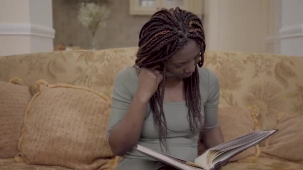 Ortrait van schattige african american vrouw met dreadlocks kijken naar de foto's in het fotoboek van de grote Lederrug met haar blote voeten omhoog. Mooie herinneringen — Stockvideo