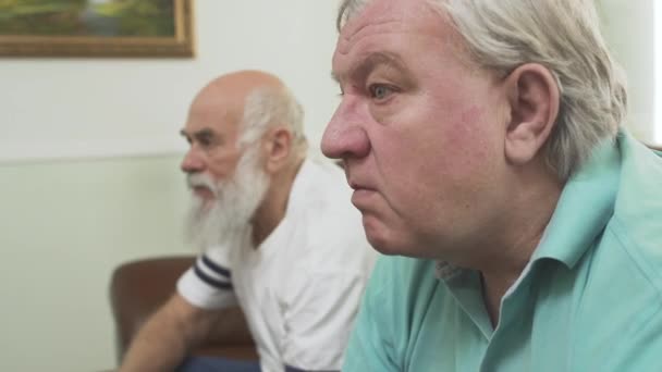 Acercamiento de dos hombres mayores maduros viendo la televisión en casa. Amigos viendo fútbol mientras comen papas fritas. Personas involucradas en el juego — Vídeos de Stock