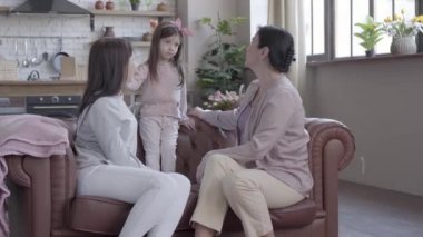 Büyükanne, anne ve küçük kızı zaman modern daire içinde kanepede birlikte oturan harcamak. Kız cout, anne ve büyükanne gülümsediğini seyir ayakta. Nesil kavramı.