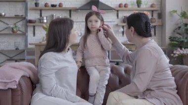 Büyükanne, anne ve küçük kızı zaman stüdyo dairede kanepede birlikte oturan harcamak. Anne ve büyükanne ona bakarken cout üzerinde duran kız. Çocuk gülümsüyor.