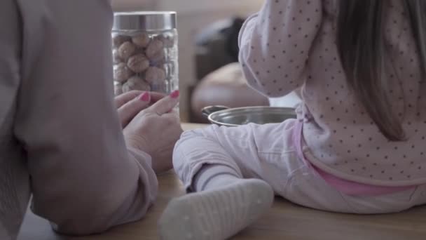 Vista posterior de la mujer y el niño pequeño sentado en la mesa de la cocina y la madre enseñando a su hija a cocinar . — Vídeos de Stock