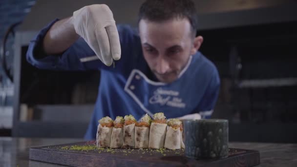 Chef cozinhar prato saboroso no restaurante moderno de perto. Homem em cozinhar uniforme polvilhando lula kebab em rolos lavash pita com tempero olhando para a comida atentamente. Cozinha turca — Vídeo de Stock