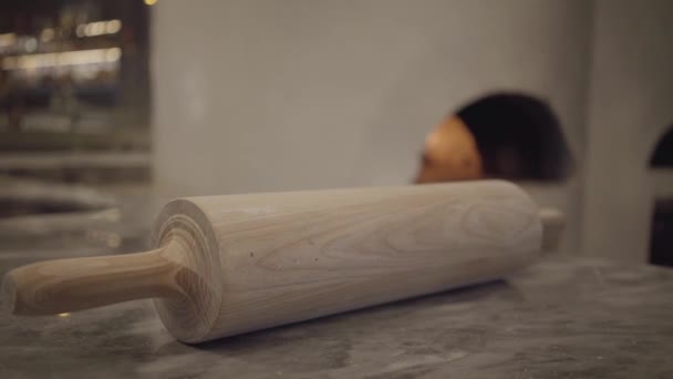 Close up view of big wooden dough rolling pin lying on the table in modern restaurant kitchen. Wood oven with fire burning inside is in the background. Food preparation concept — Stock Video