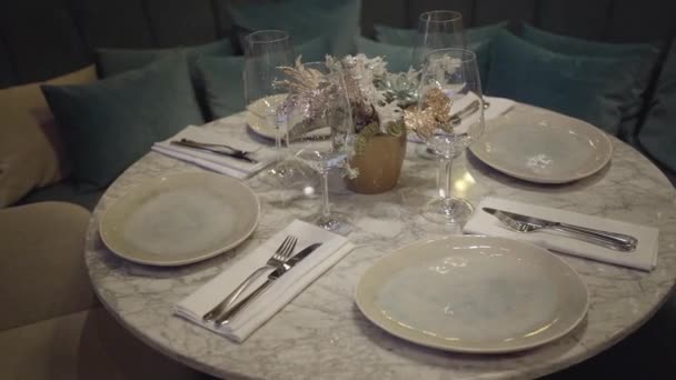 Små runda fyrsitsiga bordet väntar på sina gäster i moderna bekväma restaurang. Stor soffa med många kuddar i bakgrunden. Mat servering koncept — Stockvideo