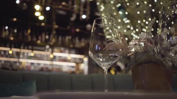 Pusty kieliszek do wina stojący na stole w restauracji obok kwiat w doniczce. Z bliska. — Wideo stockowe