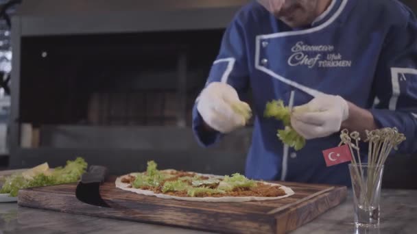 Uomo in uniforme cuoco preparare gustoso piatto avvolto in lavash. Chef mano in guanti di gomma bianca strappa foglie di lattuga e li mette sopra pita. Cucina turca — Video Stock