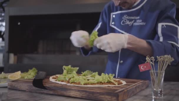 Επιδέξιος άνθρωπος με τη στολή του μάγειρα προετοιμασία νόστιμο πιάτο τυλιγμένο σε πίτας. Σεφ χέρι λευκό καουτσούκ γάντια δάκρυα μαρούλι φύλλα και τα τοποθετεί πάνω από την πίτα. Τουρκική κουζίνα — Αρχείο Βίντεο