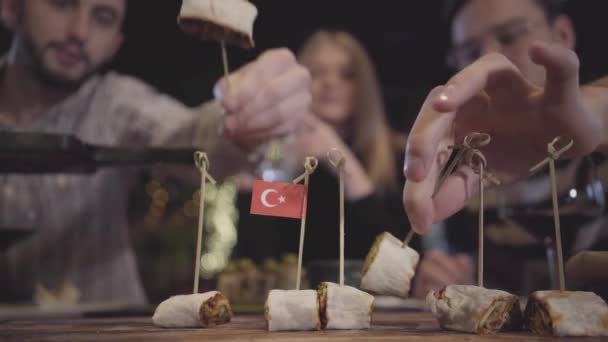 Mãos de pessoas desfocadas tomando pedaços de kebab rolou no pita deitado no tabuleiro com palhas estucadas com pequena bandeira turca. Homem alimentando mulher. Amigos têm reunião, relaxando juntos — Vídeo de Stock