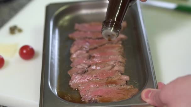 Szef kuchni strony odlewania plasterki surowe niegotowane mięso z sosem, marynować go. Kucharz, przygotowywania posiłków w kuchni. Niewyraźne czereśnie pomidory w tle — Wideo stockowe