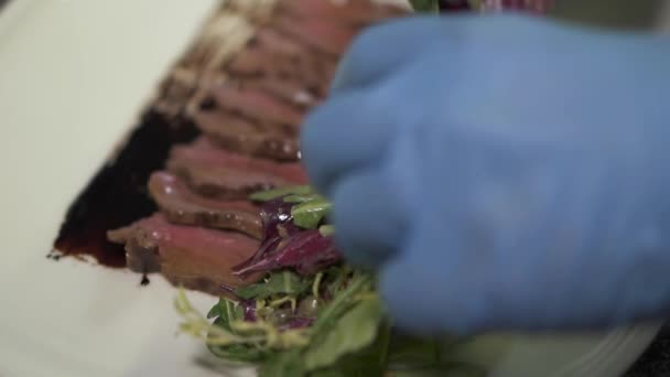 Chef mãos em luvas de borracha azul colocando salada perto do pedaço de carne cru marinado no prato de perto no restaurante moderno. Cozinhe preparando comida de carne. Estilo de vida saudável — Vídeo de Stock