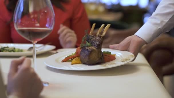 Camarero irreconocible sirviendo plato grande con costillas asadas con verduras a la parrilla de cerca. Hombre y mujer teniendo una cita en un lugar cómodo, ordenando comida sabrosa con alcohol — Vídeo de stock