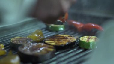 Şef el dönüm diğer yan sebze domates patlıcan, kabak, sarı dolmalık biber ızgara metal maşa kullanarak kapatın. Cook vejetaryen yemek hazırlanıyor. Sağlıklı yaşam tarzı